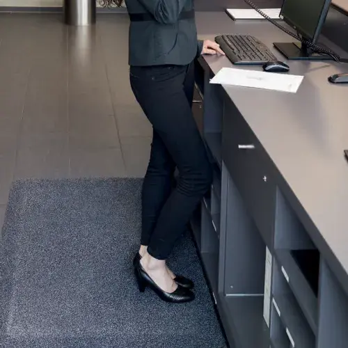 Eine Frau steht auf einer CWS Gesund-Stehen-Matte am Arbeitsplatz