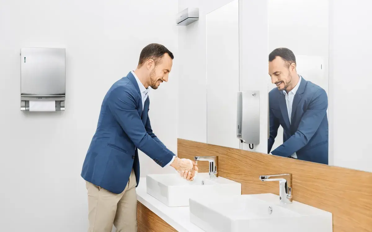 Ein Mann wäscht sich die Hände in einem mit CWS Produkten ausgestatteten Bad.