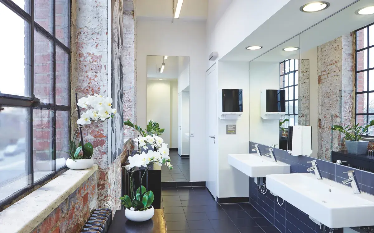 Waschraum mit Waschbeckenzeile, Wandspiegeln, sowie Seifen- und Handtuchspender von CWS.