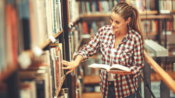 Junge Frau stöbert in Bibliothek nach Büchern