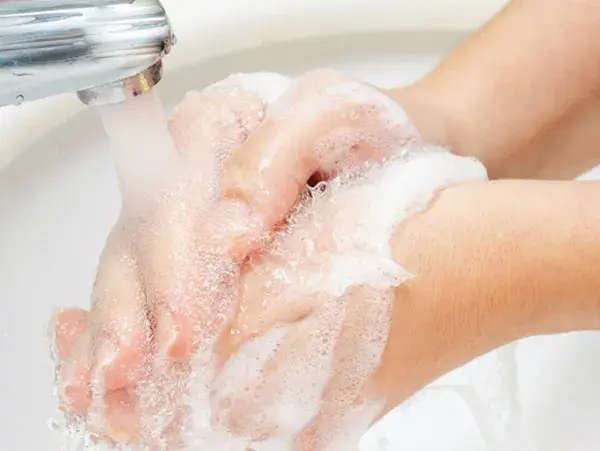 Două mâini săpunite se clătesc sub jet de apă.